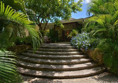 The main entrance leads through a welcoming hall straight into to an open-plan sitting living room with three sets of large double doors opening out behind the house into a courtyard planted with frangipani and ginger lilies.